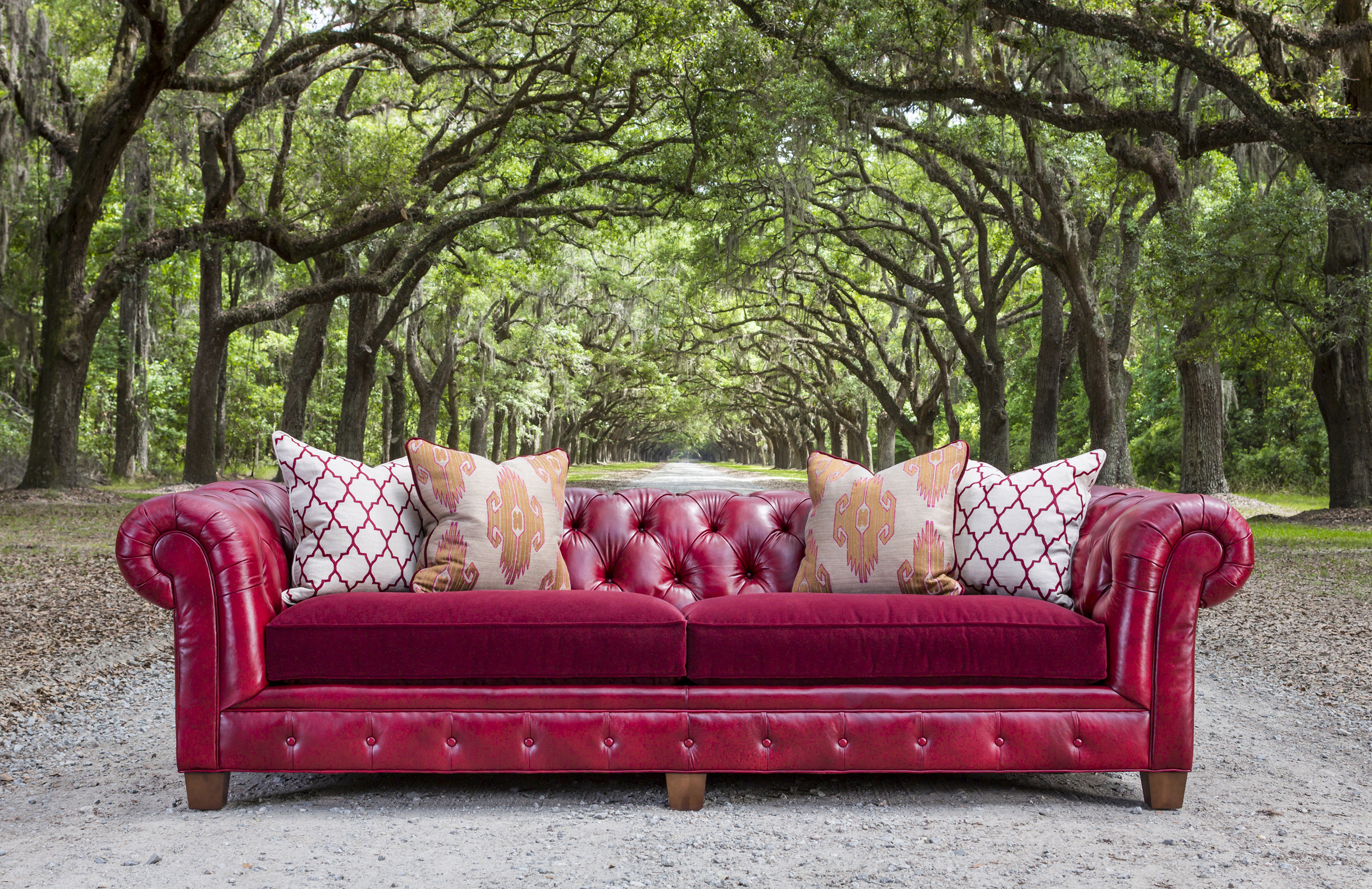 red leather chesterfield sofa with red cloth cushions photographed on a dirt road with a tree canopy arching over